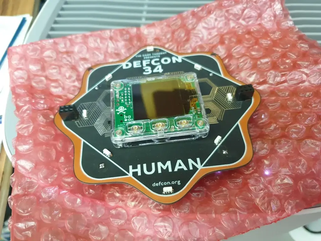 Acreditación electrónica Human de DEF CON 34 con pantalla y placa de circuito