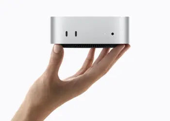 Un Mac mini plateado sostenido con una mano sobre fondo blanco