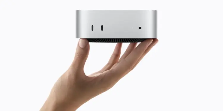 Un Mac mini plateado sostenido con una mano sobre fondo blanco