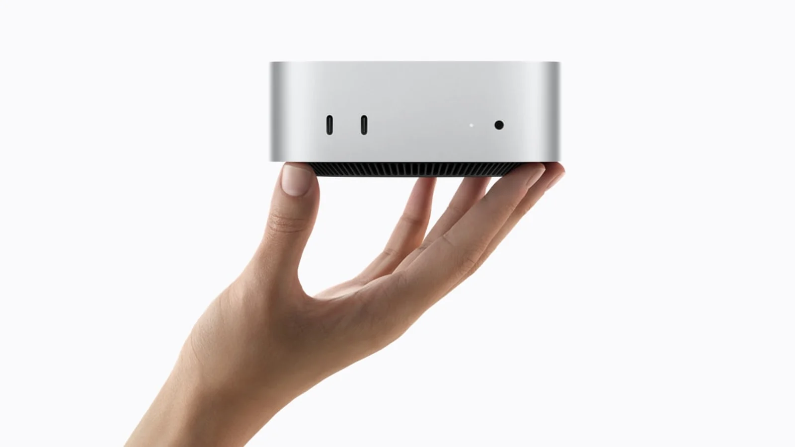 Un Mac mini plateado sostenido con una mano sobre fondo blanco